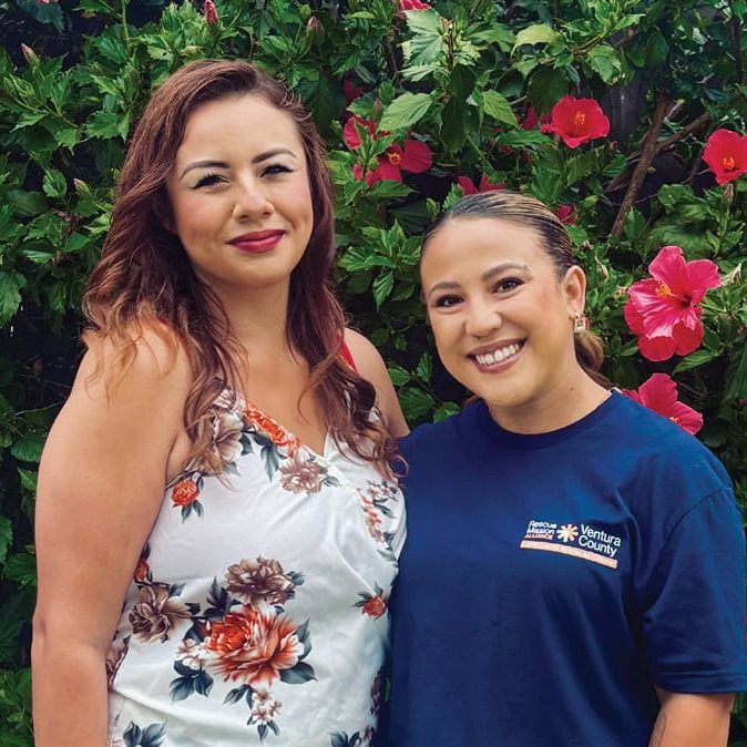 Rescue Mission Alliance Ventura County staff member with a woman in front of pink hibiscus flowers.