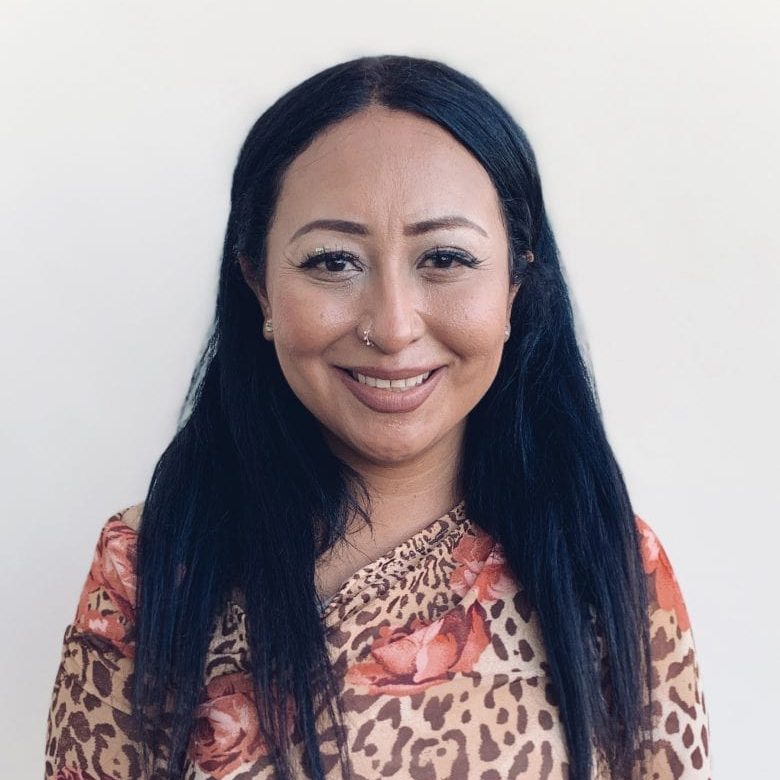 Portrait of a smiling woman with long dark hair against a light background.