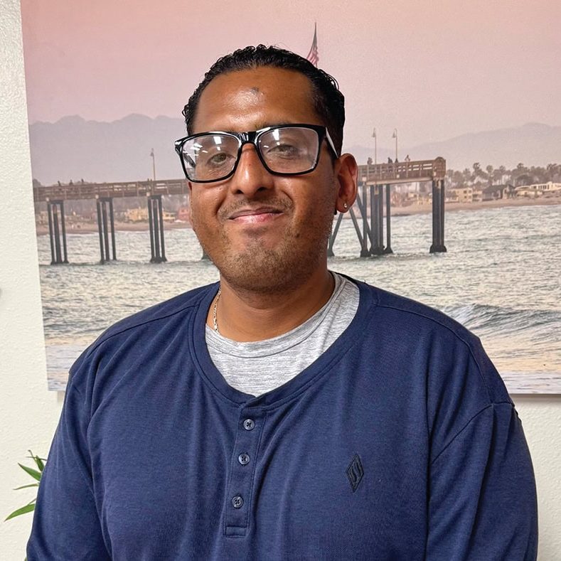 A man smiling indoors with a waterfront mural in the background, representing Rescue Mission Allianc.