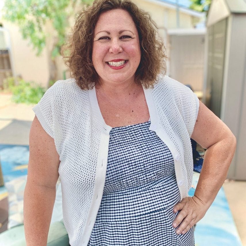 Smiling woman outdoors at Rescue Mission Ventura County with greenery and shed in background.