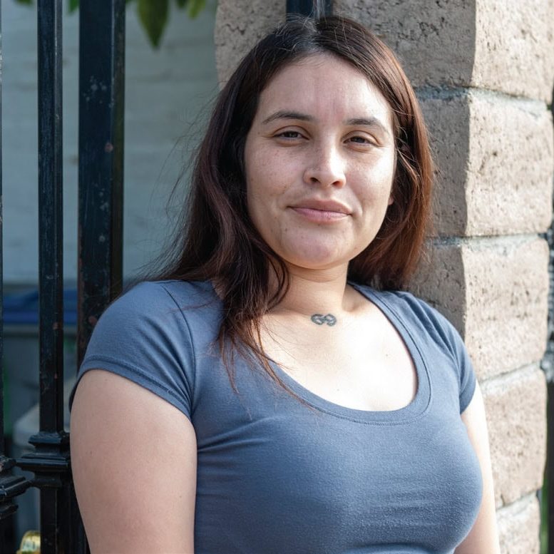 Young woman standing outdoors near a brick wall and black fence.